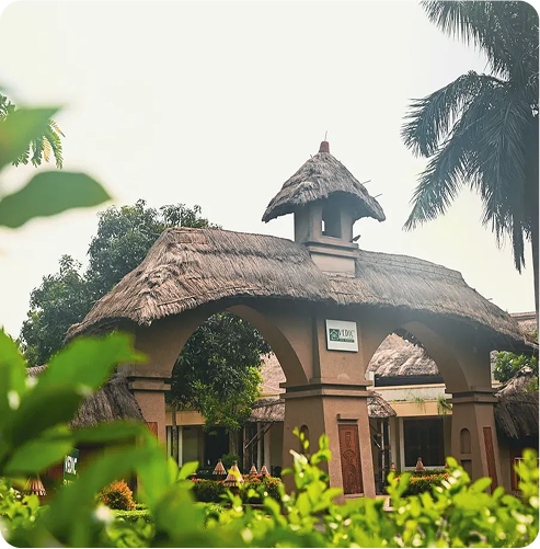 Entrance of Vedic Village with thatched roof gate surrounded by greenery